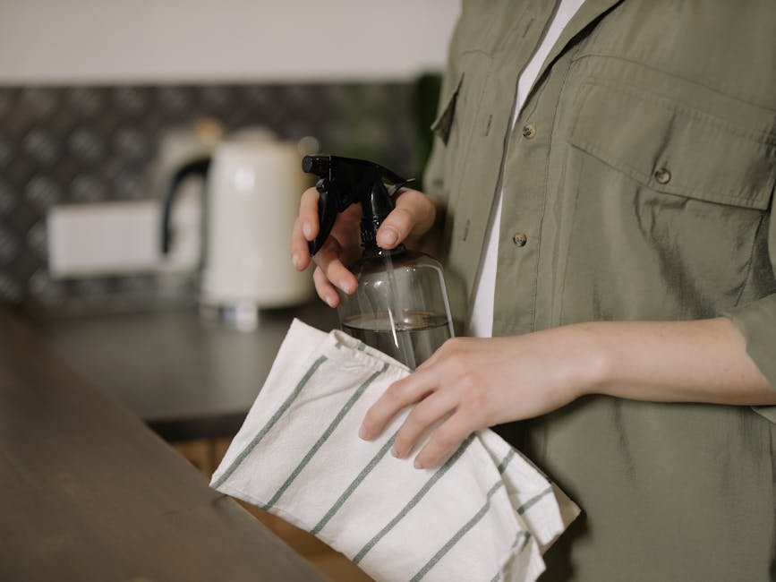 A person cleaning a kitchen counter with a spray bottle and cloth, maintaining cleanliness.