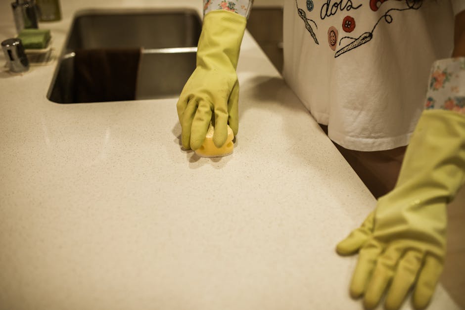 Woman using yellow rubber gloves to clean a kitchen counter with a sponge.